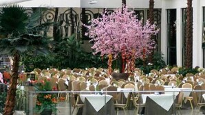 A banquet hall with round tables and chairs, a large decorative tree, and a patterned wall in the background. - Hot Spring Hotel (Beijing)