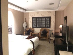 Une chambre d’hôtel avec un grand lit, deux fauteuils, une télévision et un paravent décoratif au mur.