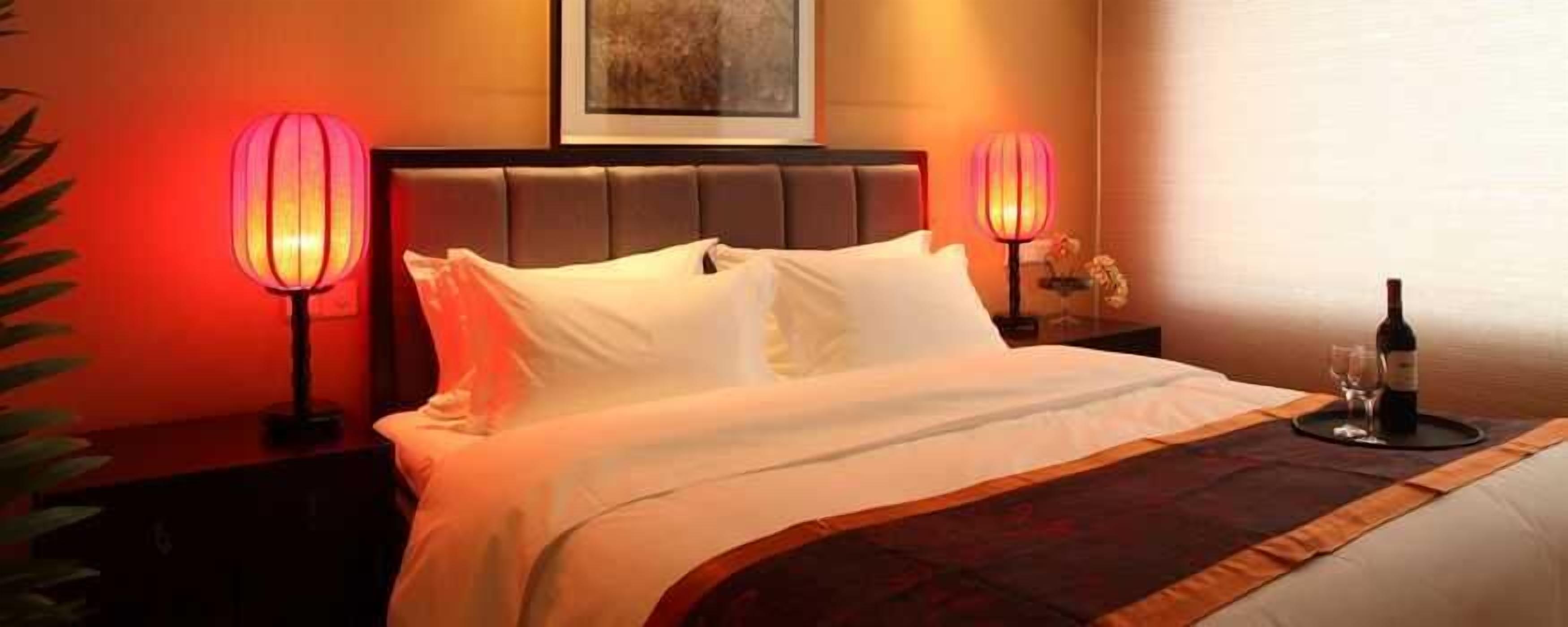 Habitación de hotel con una cama, dos lámparas de noche, una botella de vino y una copa sobre una bandeja.