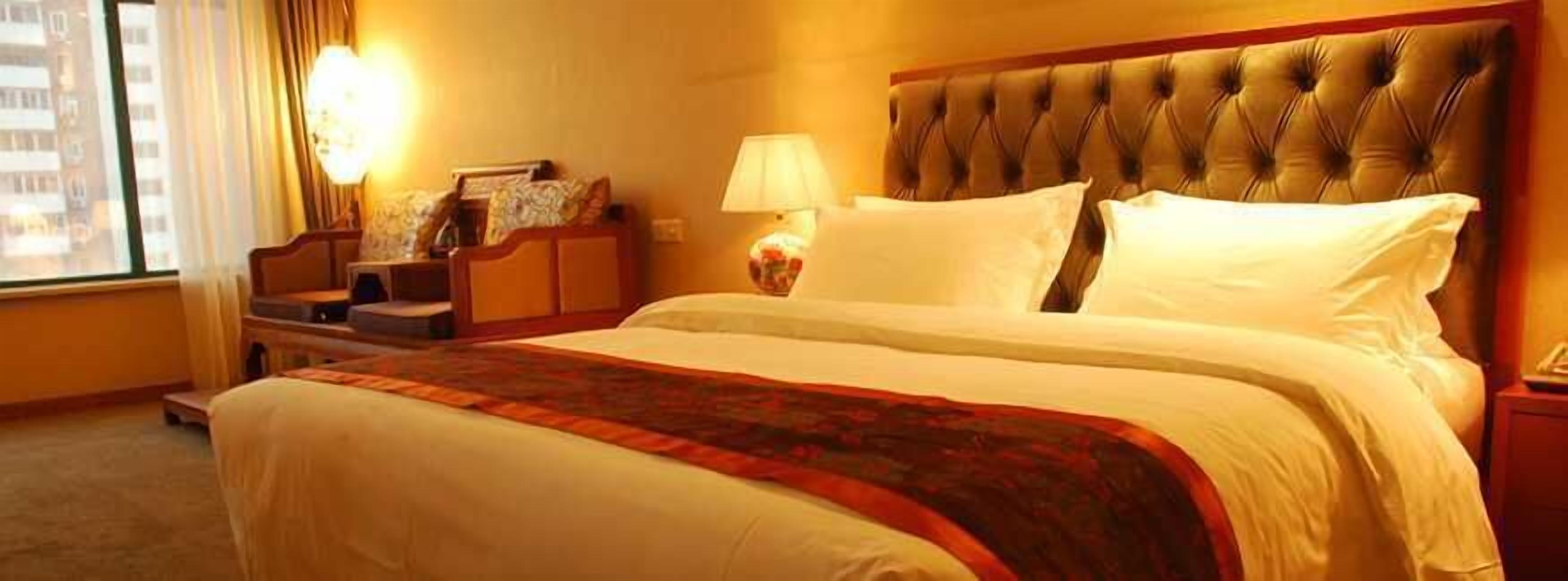 A hotel room with a large bed, a nightstand, a lamp, and a window with curtains.