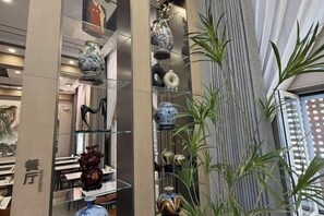 A modern interior with a glass display of decorative items, a vertical striped wall, and a plant. - Hejia Inn (Beijing Tsinghua) (Beijing)