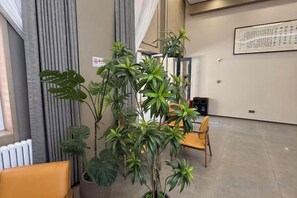 A room with a large potted plant, a chair, a radiator, and a wall-mounted artwork. - Hejia Inn (Beijing Tsinghua) (Beijing)