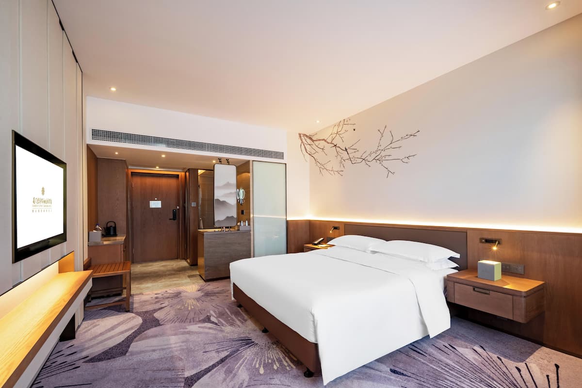 Una habitación de hotel con cama, mesita de noche, televisión montada en la pared y un elemento decorativo en la pared.