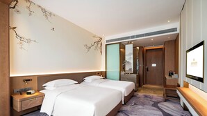 Habitación de hotel con dos camas, televisión, mesita de noche, espejo y baño visible a través de una puerta abierta.