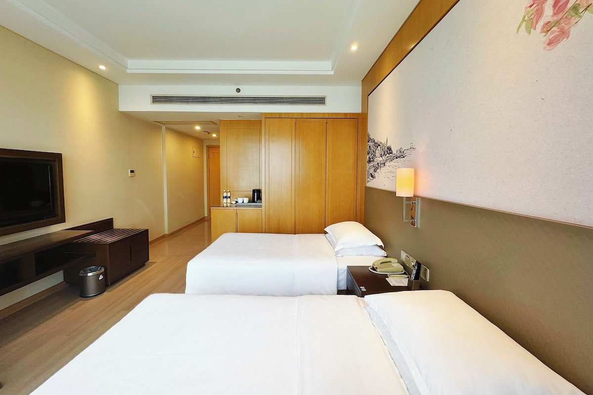 Habitación de hotel con dos camas, televisión, kitchenette pequeña y un cuadro en la pared.