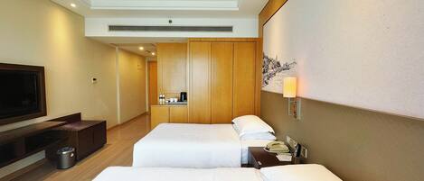 A hotel room with two beds, a TV, a small kitchenette, and a painting on the wall.