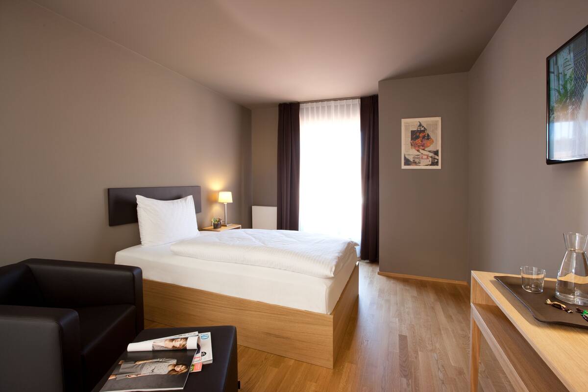 A hotel room with a bed, a desk, a chair, and a window with curtains.