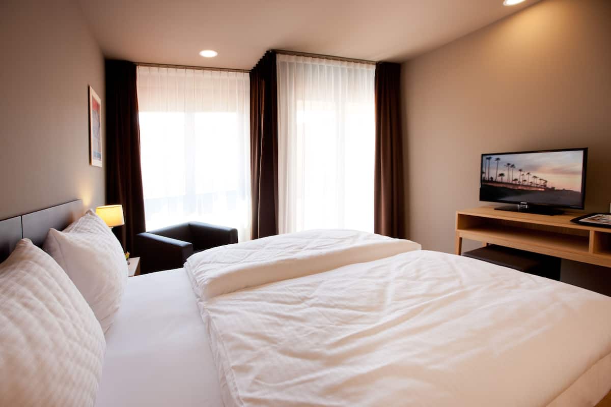 A hotel room with a large bed, a desk with a television, and a window with curtains.