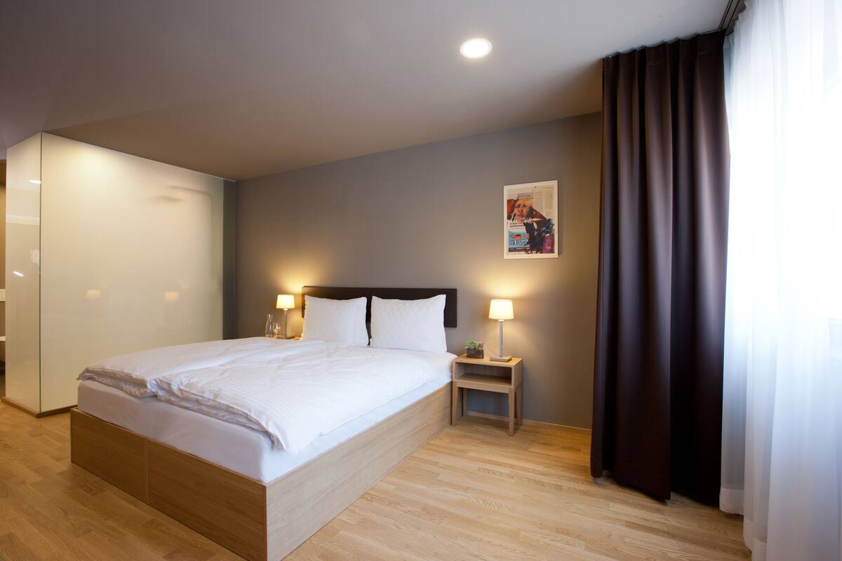 A modern hotel room with a large bed, bedside lamps, a nightstand, and a painting on the wall.