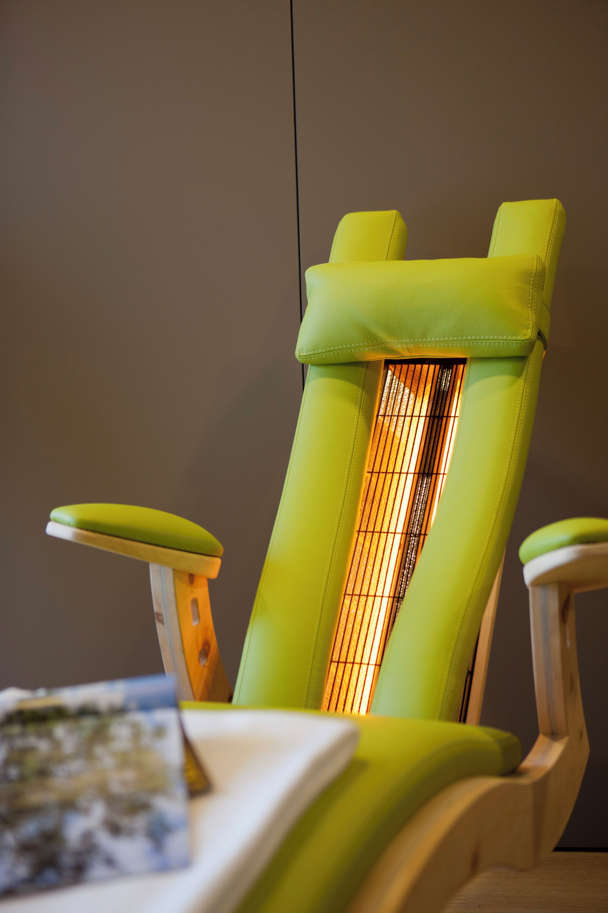 A chair with a backrest and armrests, a table with a book, and a wall.