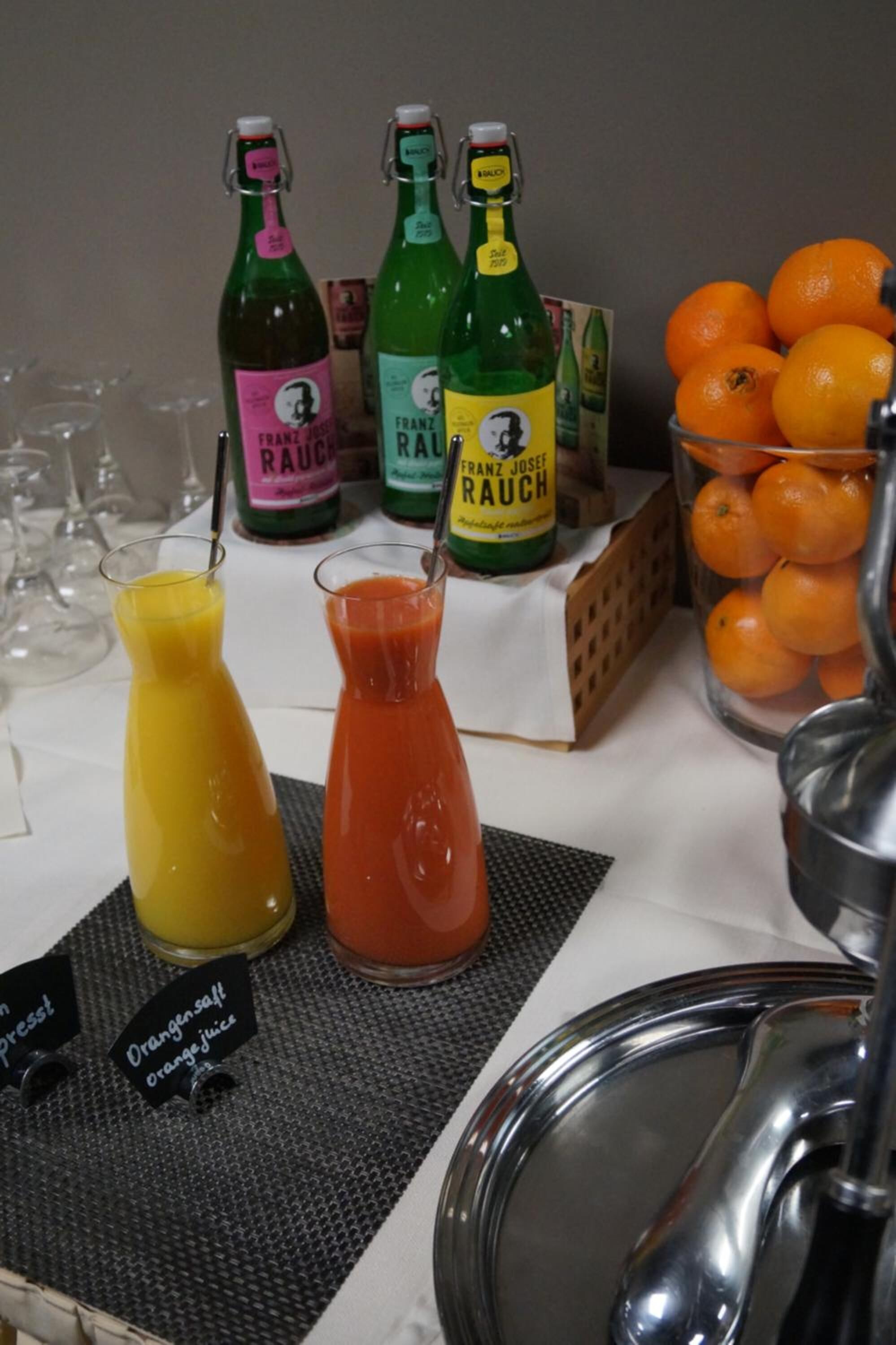 Estación de bebidas con dos botellas de jugo de naranja y dos vasos de jugo.