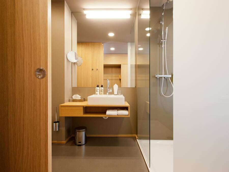 Un baño moderno con tocador de madera, cabina de ducha de vidrio y un cubo de basura visible.