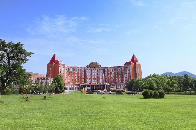A large red building with a central dome and two towers, surrounded by a well-maintained lawn and trees.