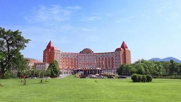 A large red building with a central dome and two towers, surrounded by a well-maintained lawn and trees.
