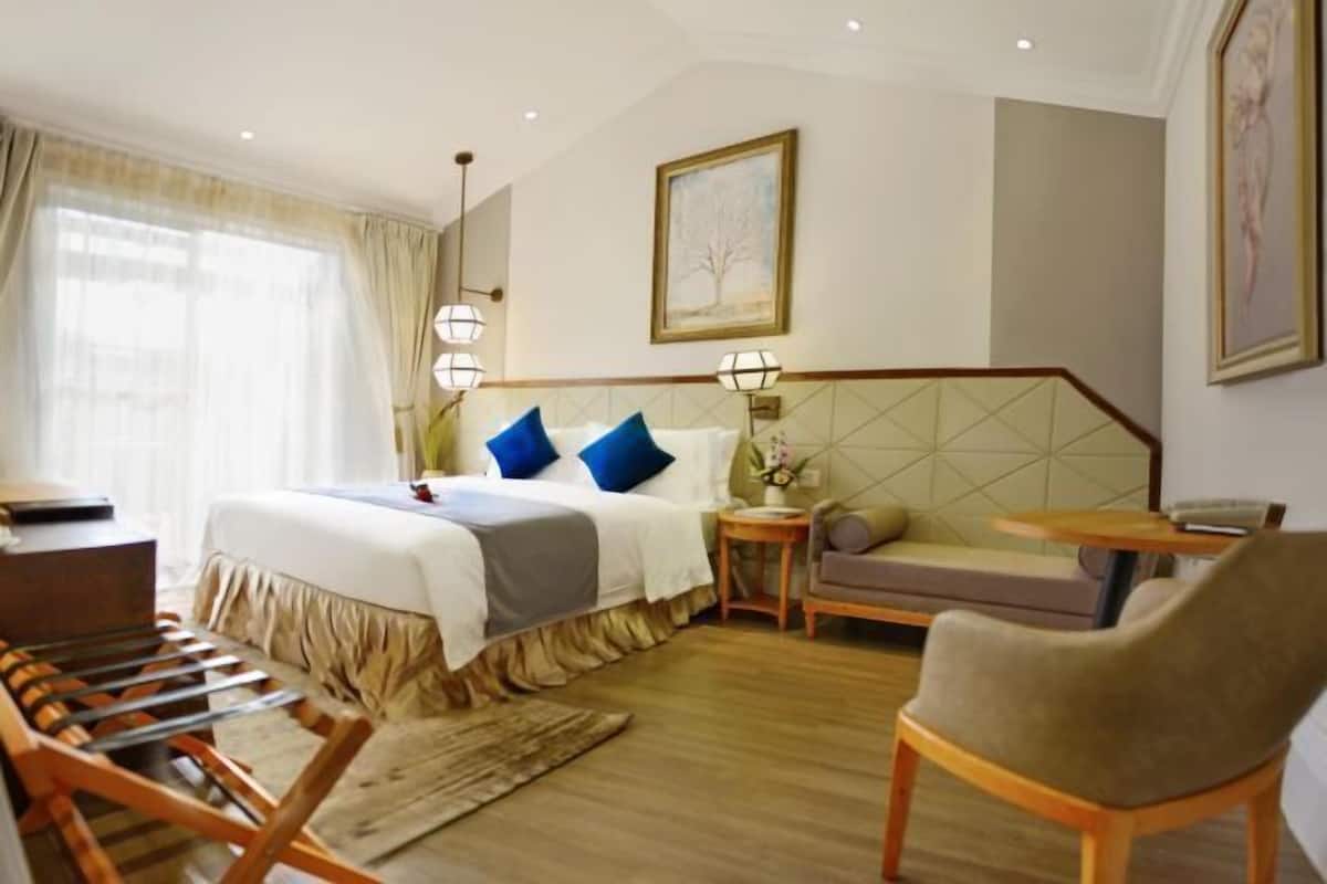 A hotel room with a bed, a sofa, a chair, a small table, and a nightstand.