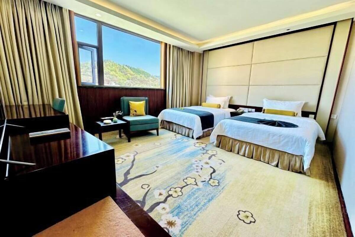 A hotel room with two beds, a desk, and a view of the outdoors.