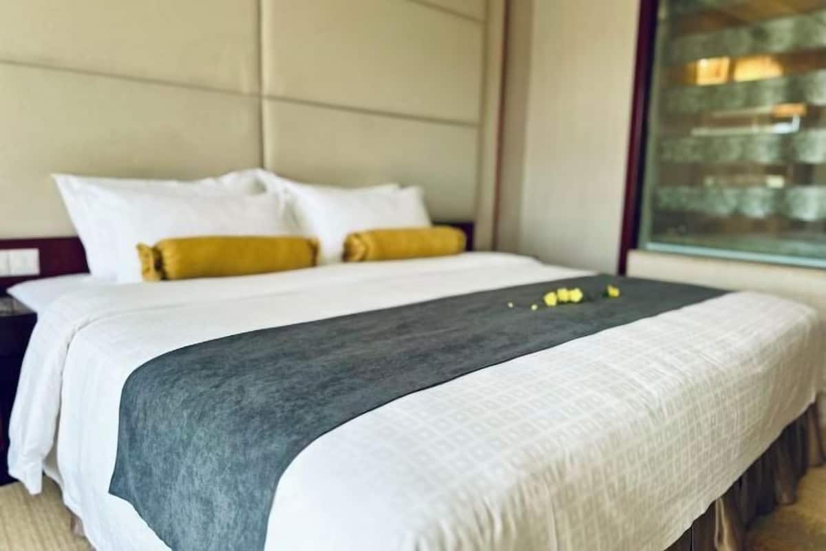 A neatly made bed with white and gray bedding, two pillows, and a dark gray throw blanket.