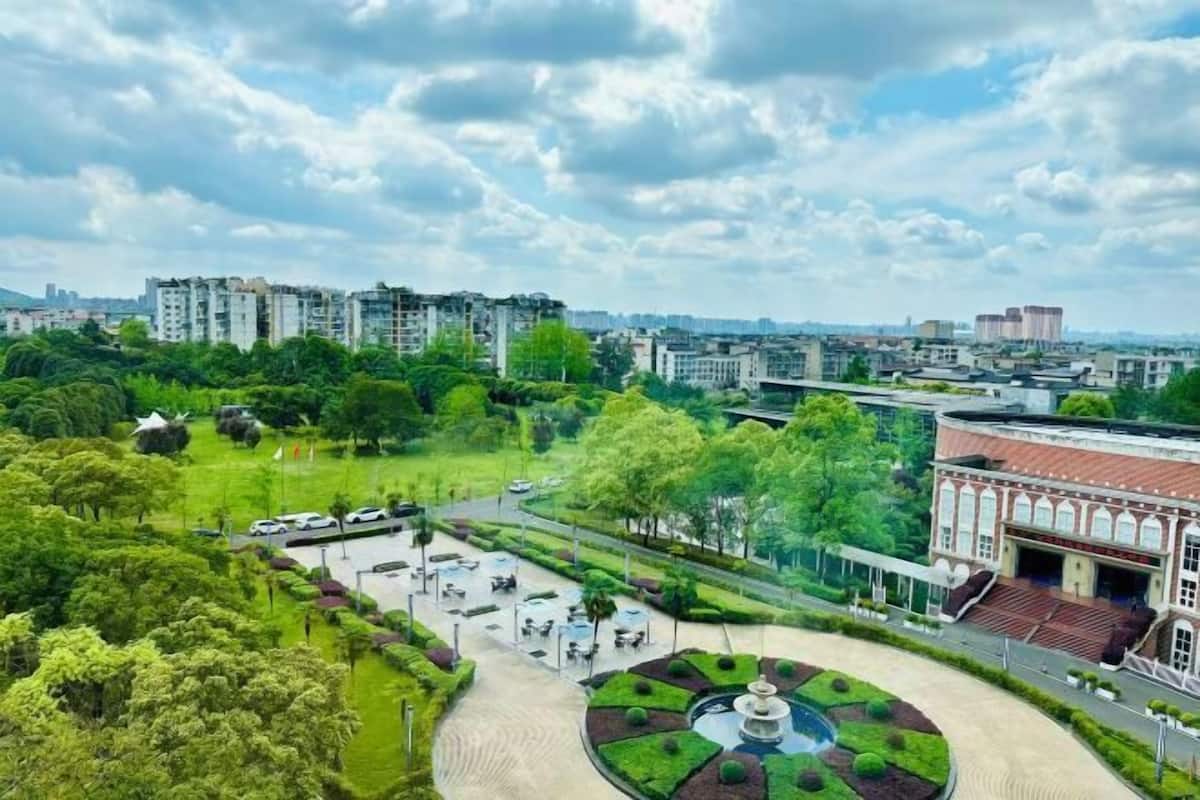 A park with a fountain, surrounded by greenery and buildings.