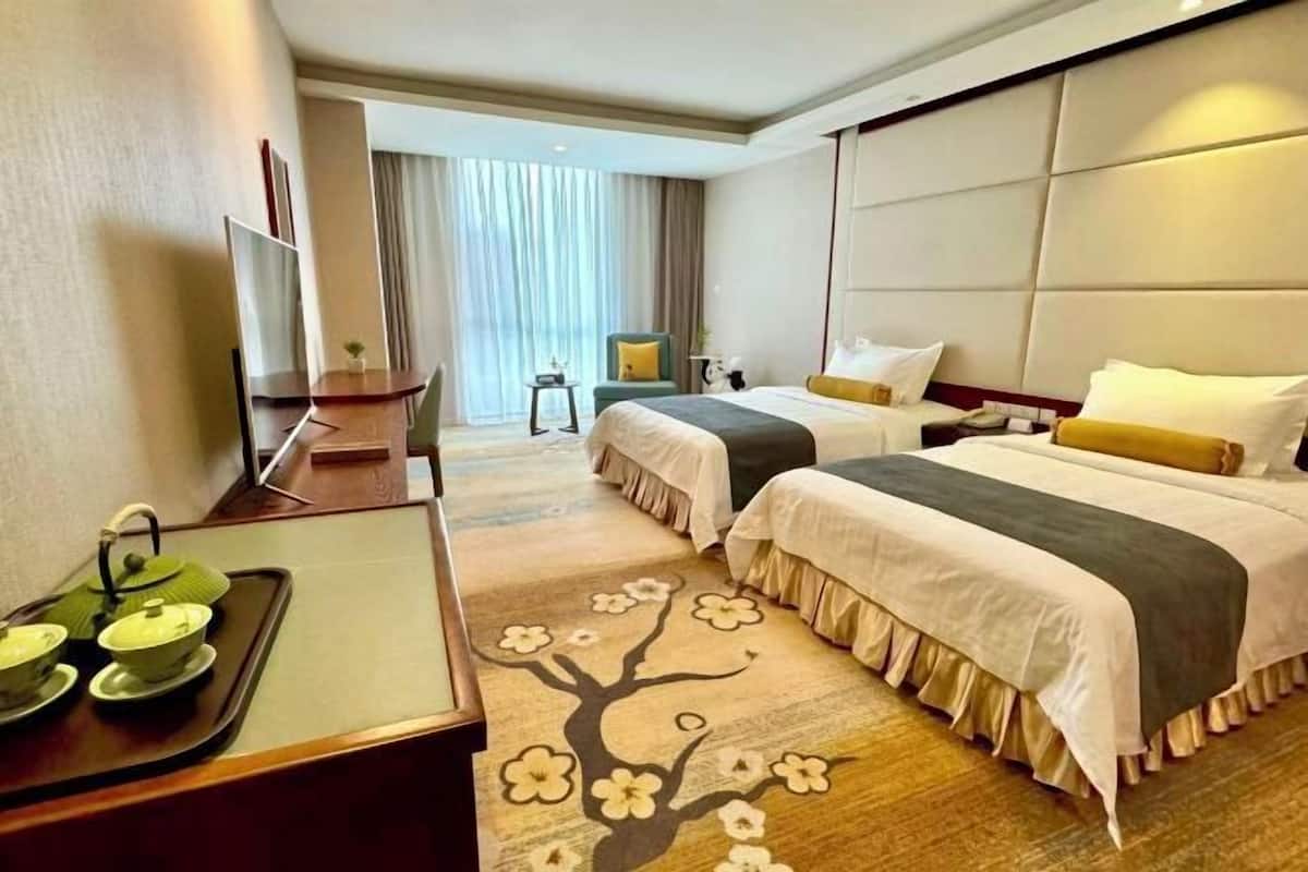 A hotel room with two beds, a desk with a tray of tea, and a view of the city through large windows.