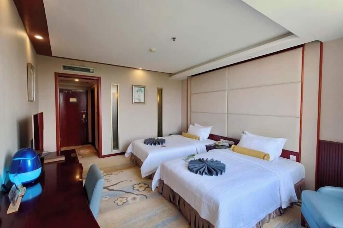 A hotel room with two beds, a desk, and a chair.