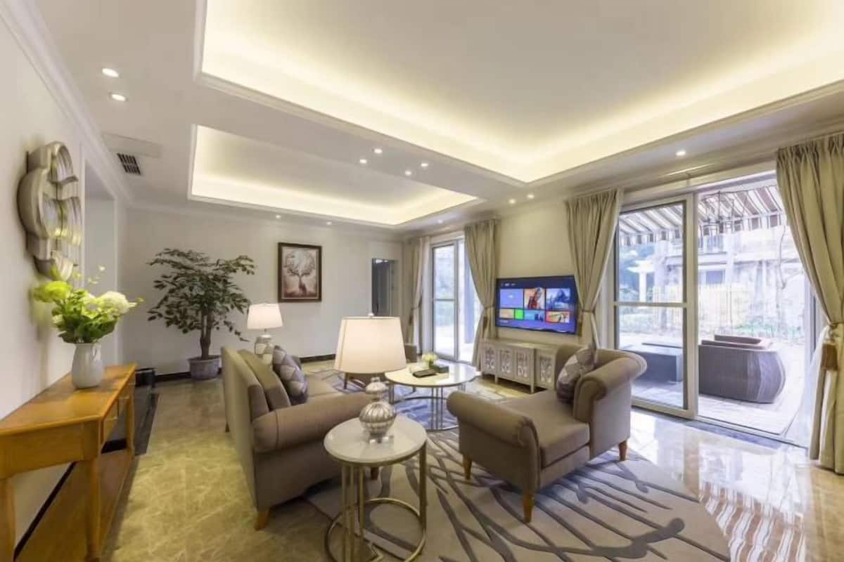 A modern hotel room with a sofa set, a TV, a lamp, and a large window with curtains.