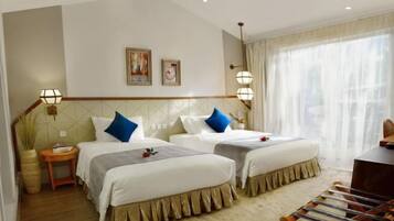 A hotel room with two beds, a small table, a chair, and a large window with sheer curtains.