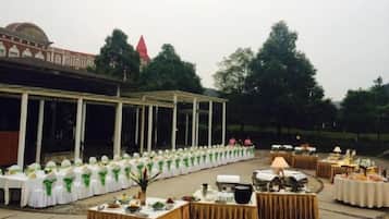 An outdoor event space with tables set for a reception, a covered area with columns, and a building with a dome in the background.