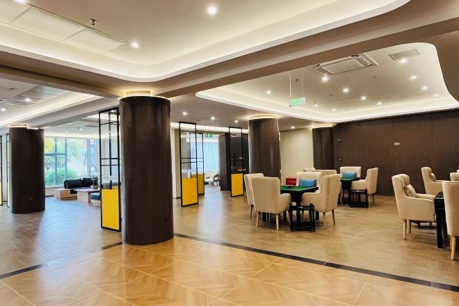 A spacious lobby with a modern design, featuring a seating area with tables and chairs, a reception desk, and large pillars.