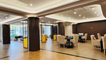 A spacious lobby with a modern design, featuring a seating area with tables and chairs, a reception desk, and large pillars.
