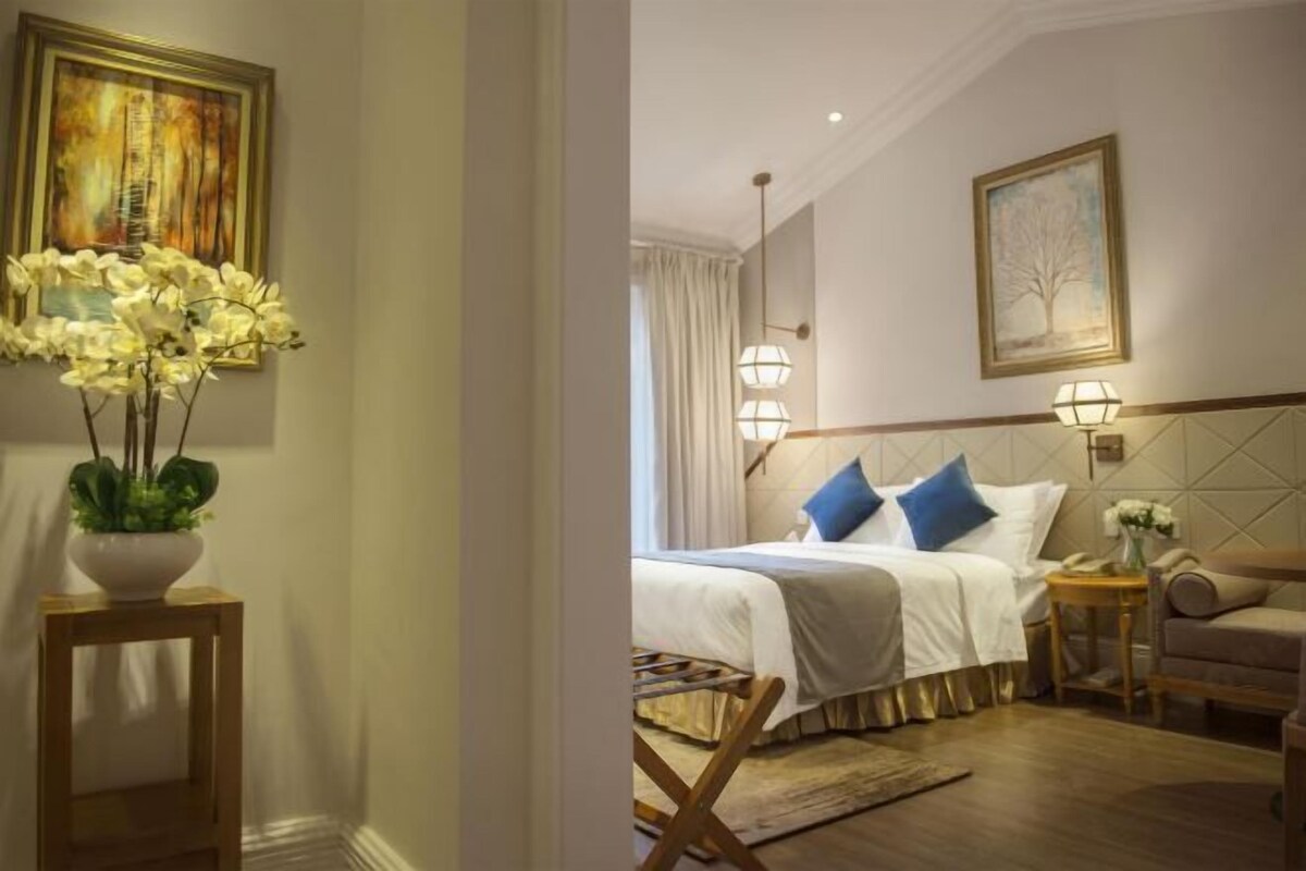 A hotel room with a bed, bedside tables, a chair, and artwork on the walls.