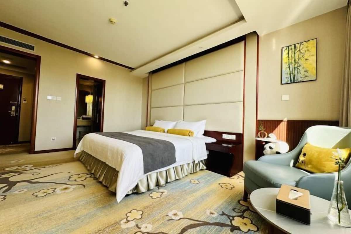 A hotel room with a bed, a sofa, a nightstand, and a painting on the wall.