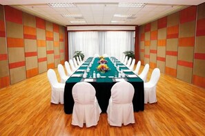 Un salón de conferencias con una larga mesa, sillas blancas y un mantel verde.