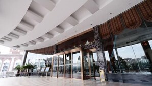 A modern hotel lobby with a curved ceiling, glass doors, and a view of the cityscape. - Brilliance Garden Hotel (CHENGDU)