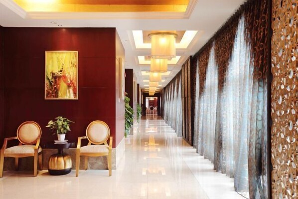 Un hall d’hôtel avec un long couloir, des chaises en bois, une plante en pot et un grand tableau abstrait accroché au mur.
