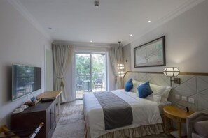 A hotel room with a bed, a desk, a chair, a TV, a window with curtains, and a balcony. - Brilliance Garden Hotel (CHENGDU)