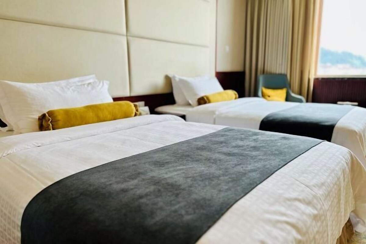 A hotel room with two beds, each with a white and grey bedspread, and a yellow pillow.