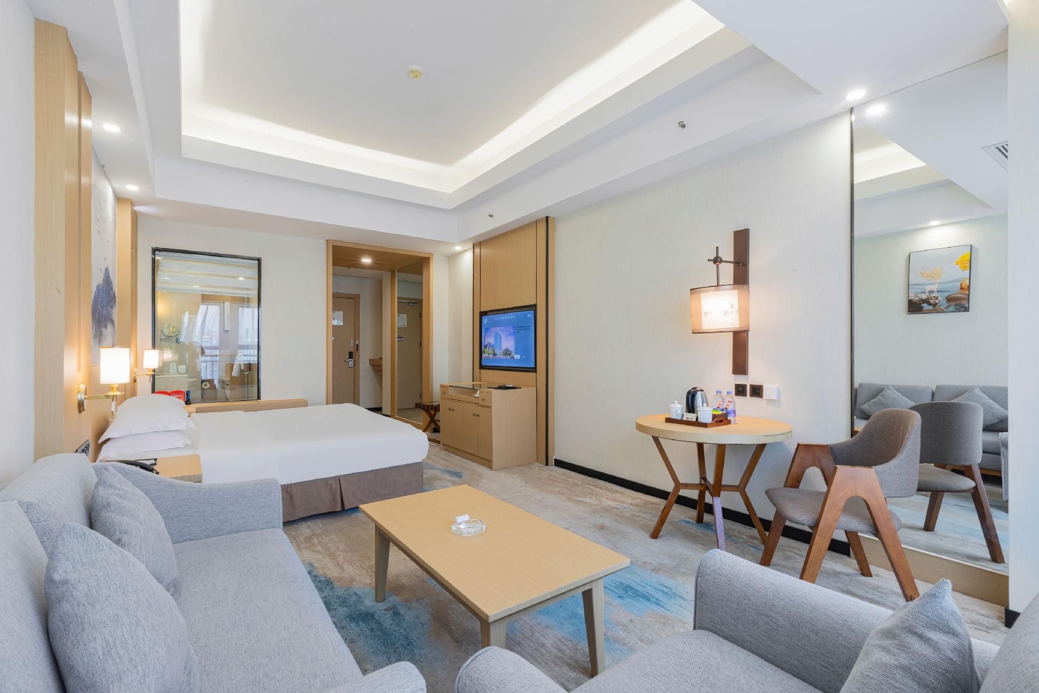 Una habitación de hotel con cama, sofá, mesa de centro, televisor y zona de comedor.