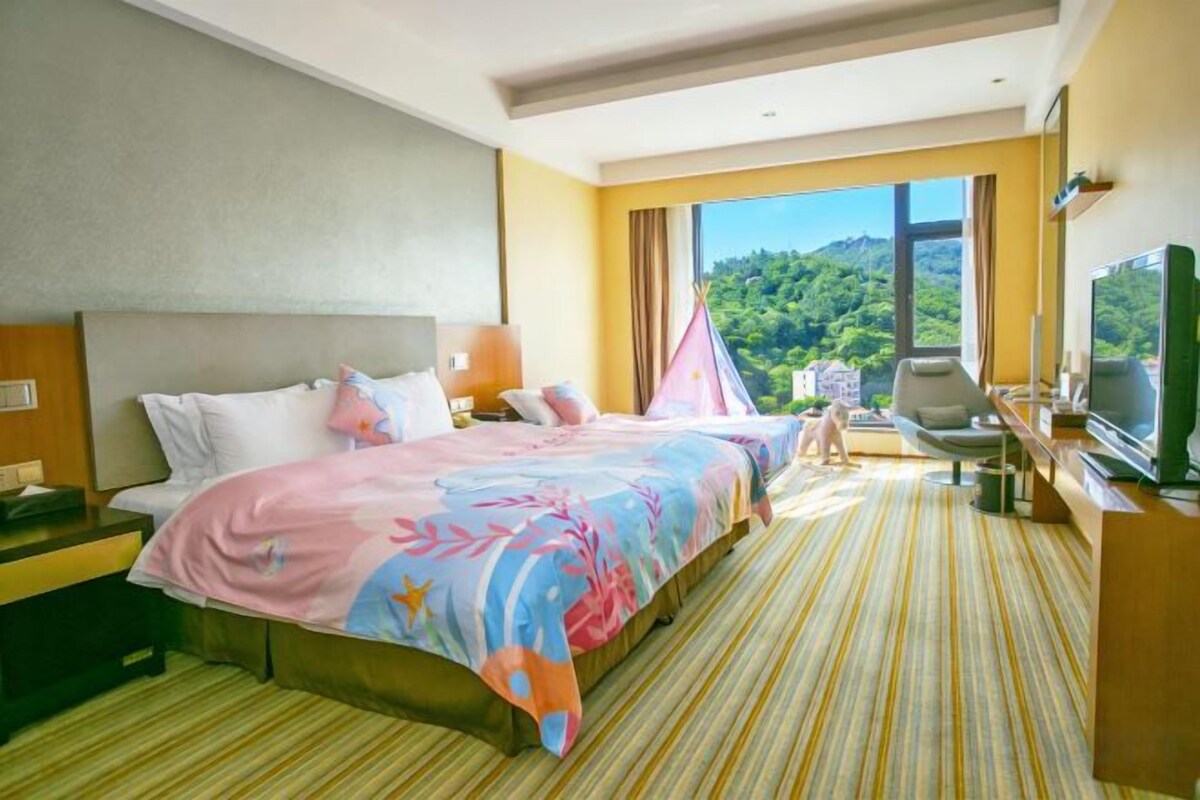 Een hotelkamer met een bed, een bureau, een televisie en een raam met uitzicht op groen.