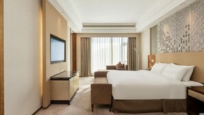 Ein Hotelzimmer mit einem großen Bett, einem Schreibtisch, einem Fernseher und Blick auf die Stadt.