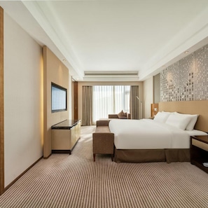 Ein Hotelzimmer mit einem großen Bett, einem Schreibtisch, einem Fernseher und Blick auf die Stadt.