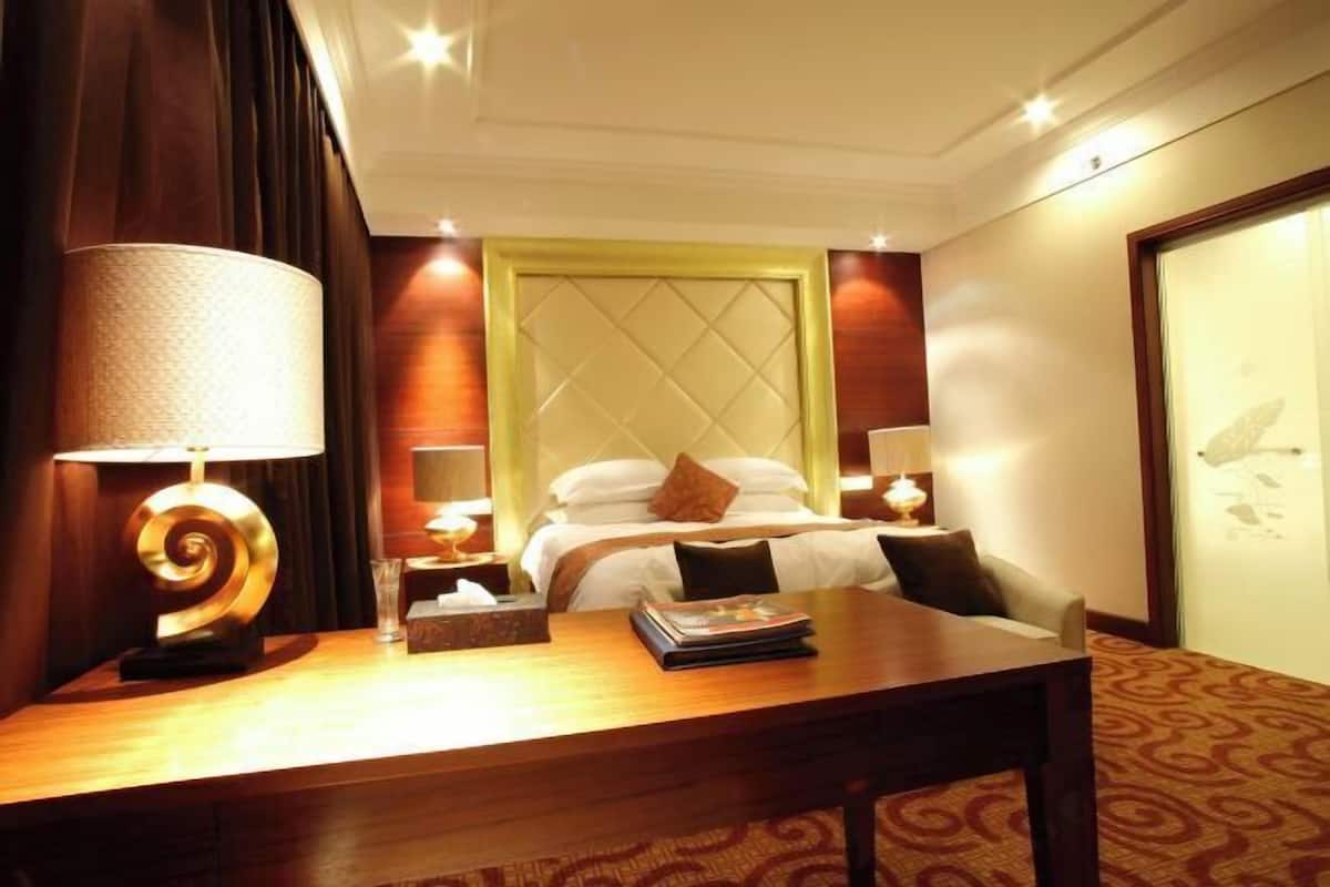 A hotel room with a bed, bedside lamps, a desk, and a nightstand.