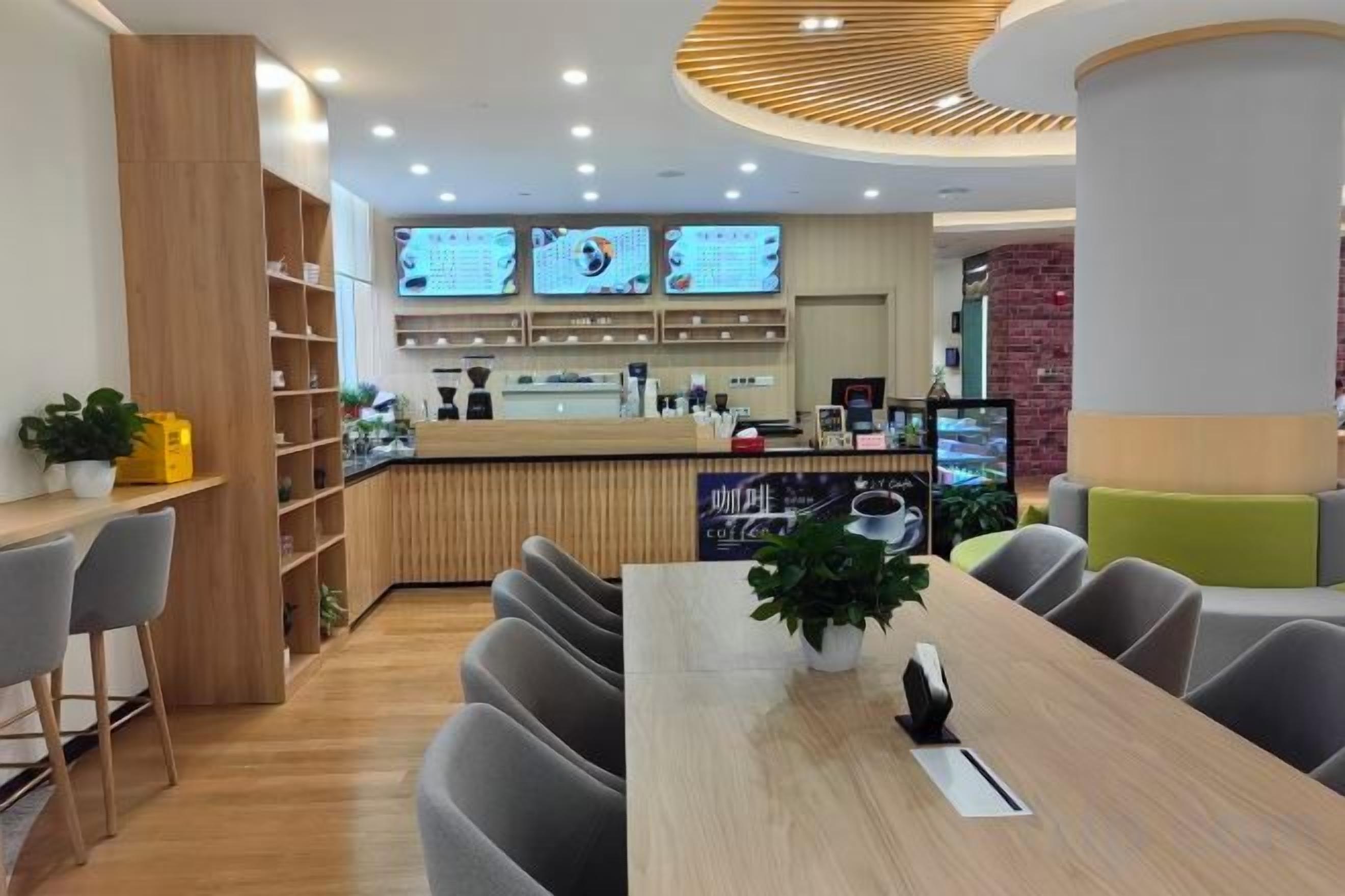 Ein modernes Café mit Holztresen, mehreren Bildschirmen zur Menüanzeige und einer Sitzgelegenheit mit Tischen und Stühlen.