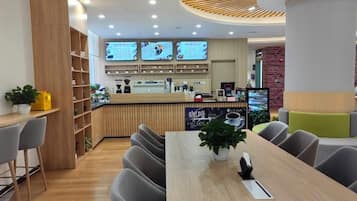 Ein modernes Café mit Holztresen, mehreren Bildschirmen zur Menüanzeige und einer Sitzgelegenheit mit Tischen und Stühlen.