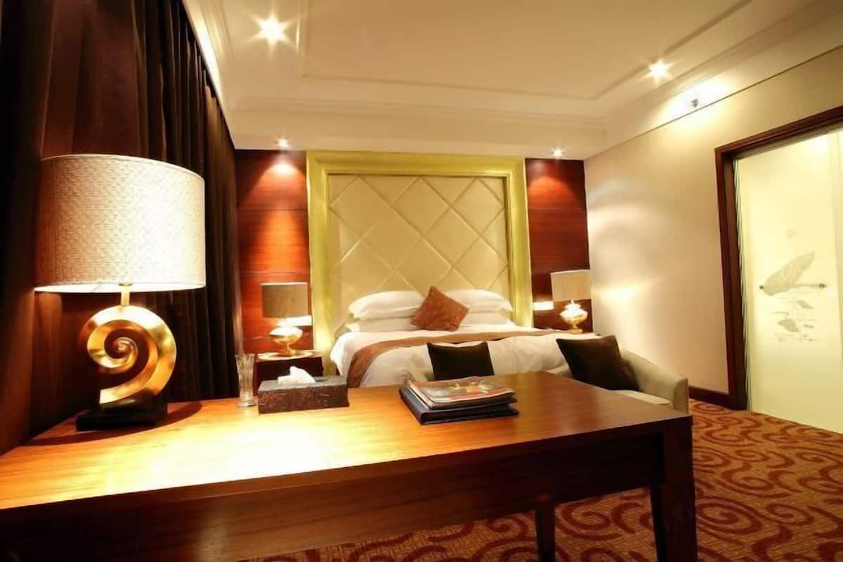 A hotel room with a bed, bedside lamps, a wooden table, and a large window.