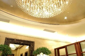 Een weelderige kroonluchter, een grote spiegel en een potplant in een hotellobby.