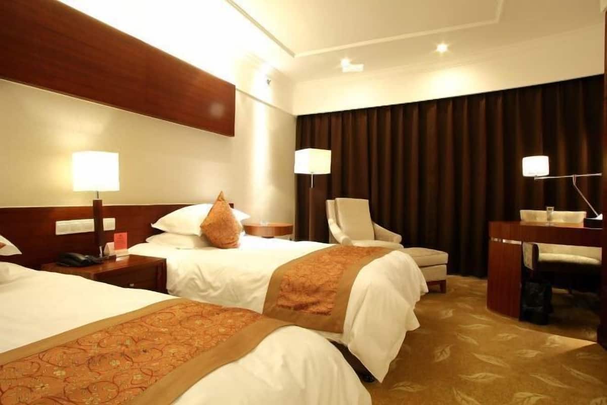 Ett hotellrum med två sängar, ett skrivbord, en stol och ett stort fönster med gardiner.