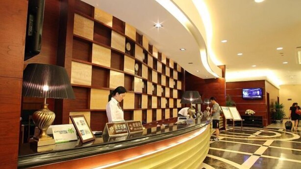 A hotel reception area with a curved counter, wooden panel wall, and a television screen above it. - Jinyan Hotel (SHANGHAI)