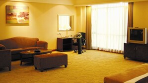 A hotel room with a sofa, a small table, a desk with a lamp, a television, and a large window with curtains. - Starshine Hotel (Shenzhen)