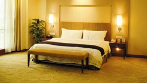 A hotel room with a large bed, a bedside table with a lamp, a nightstand with a phone, and a potted plant. - Starshine Hotel (Shenzhen)