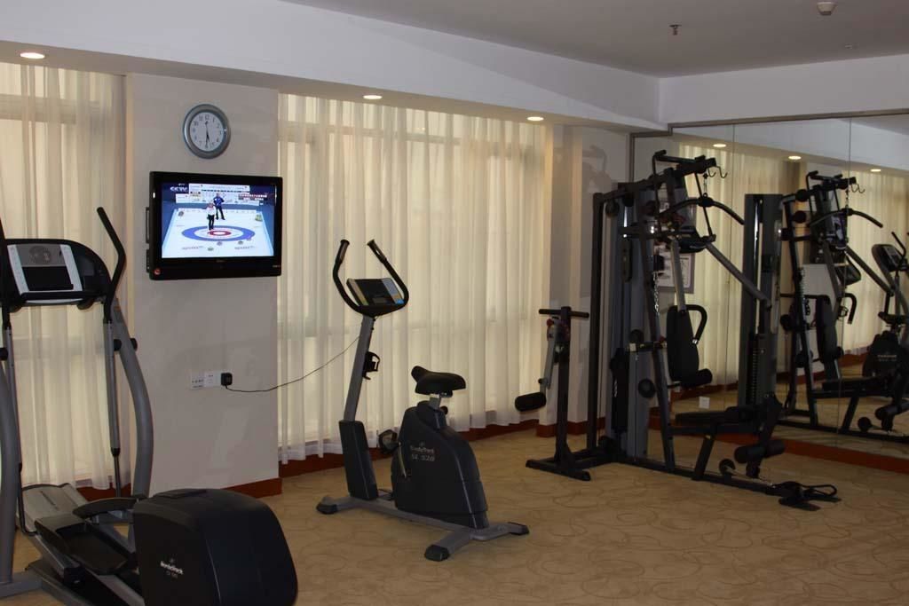 A gym with cardio machines, a TV displaying a sports event, and a mirror reflecting the equipment.